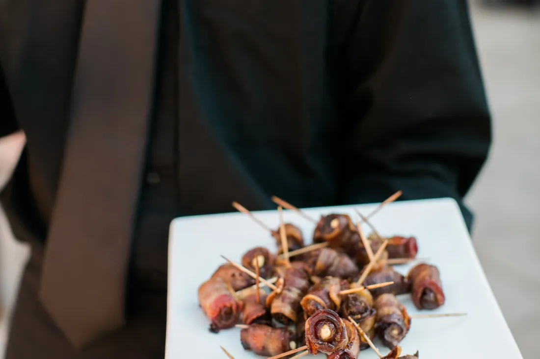 A server holding a tray of bacon-wrapped dates
