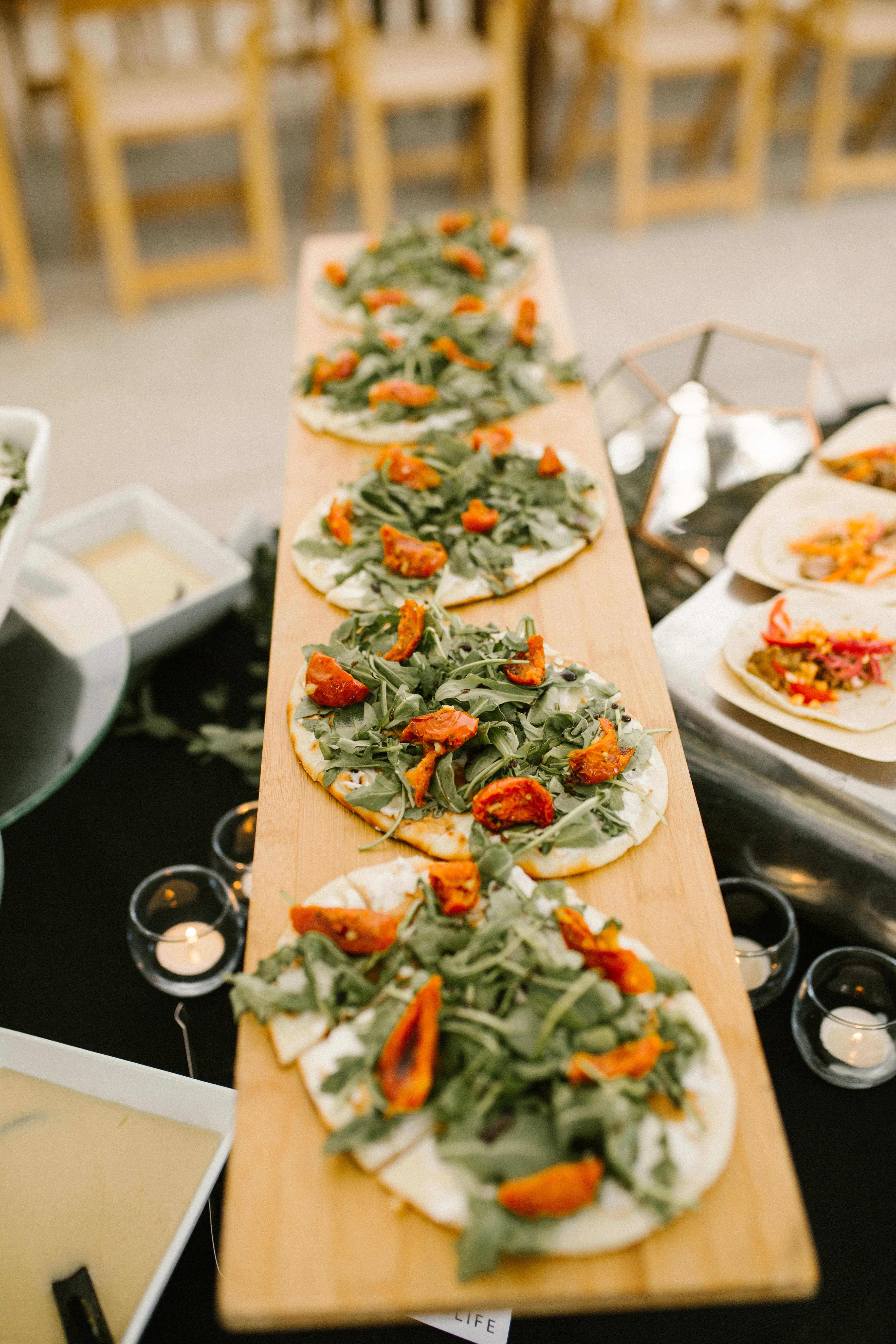 Arugula and roasted tomato flatbreads on a wooden board at a private event