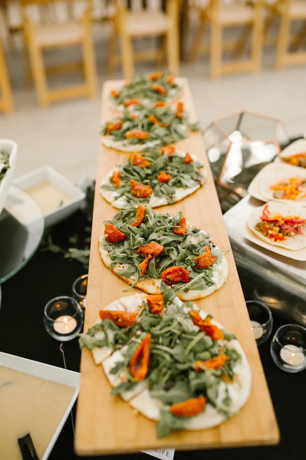 Arugula and roasted tomato flatbreads on a wooden board at a private event