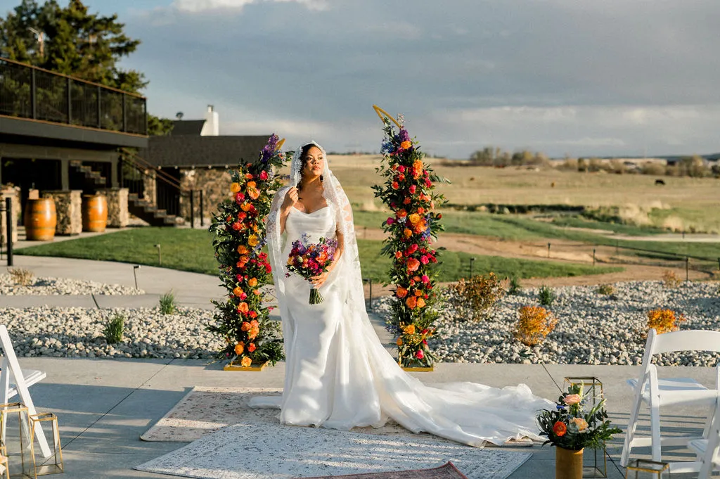 A bride beside a floral ceremony arch on the terrace at a Colorado wedding venue