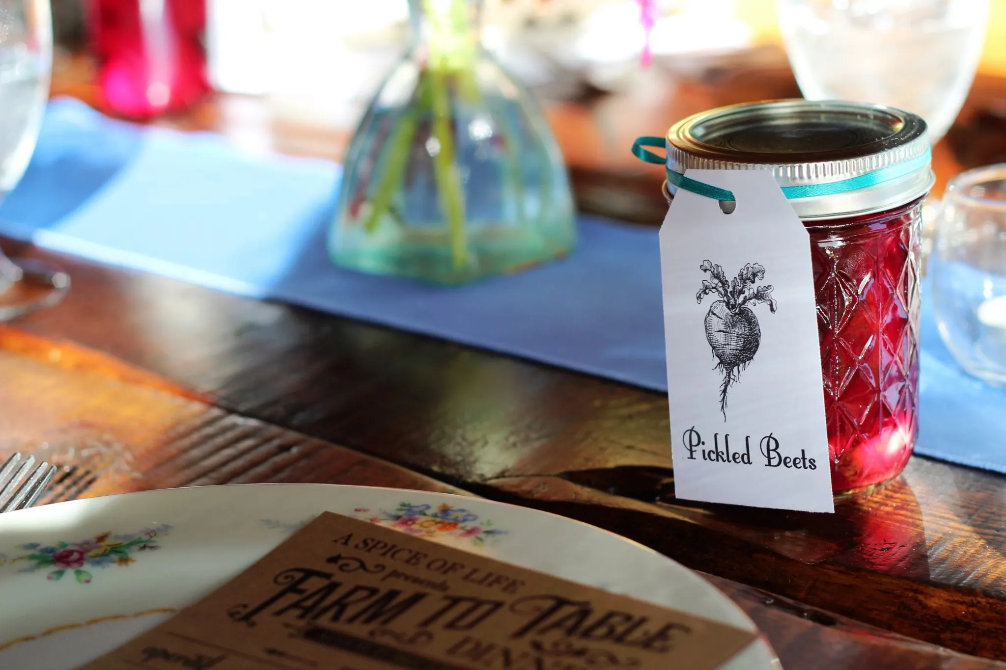 A hand-lettered menu card reading Pickled Beets beside a place setting at a farm table
