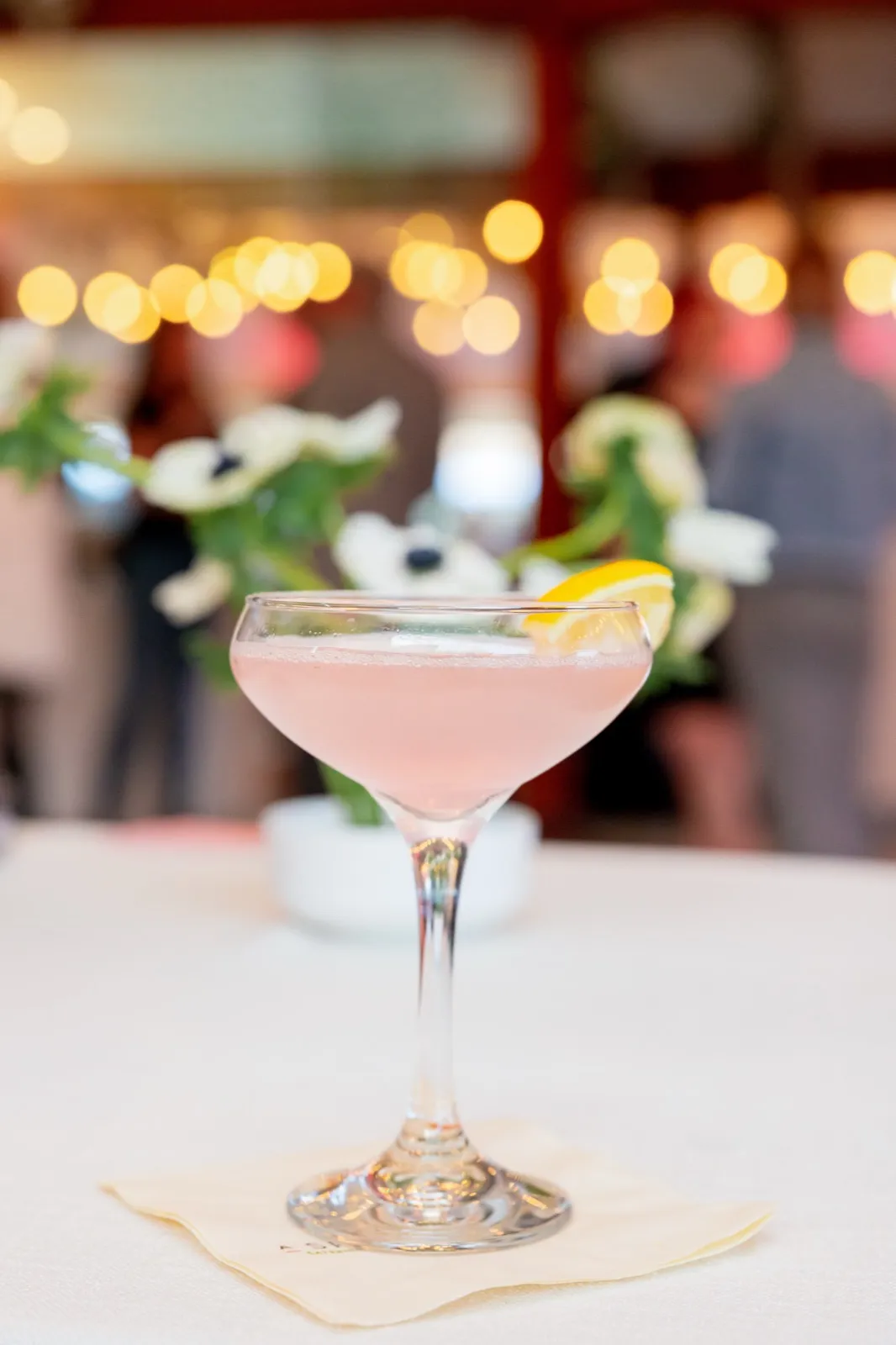 A pink coupe cocktail with a lemon twist at an evening event