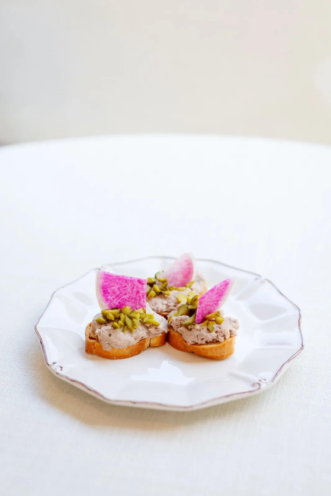 Crostini with a savory spread, pistachios, and watermelon radish on a white plate