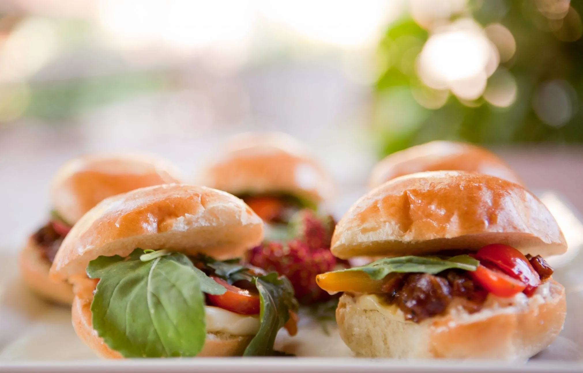 Brioche sliders with basil and tomato lined up on a serving board